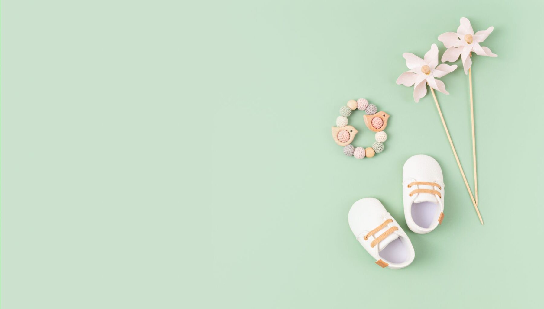 New baby shoes and toys against green background