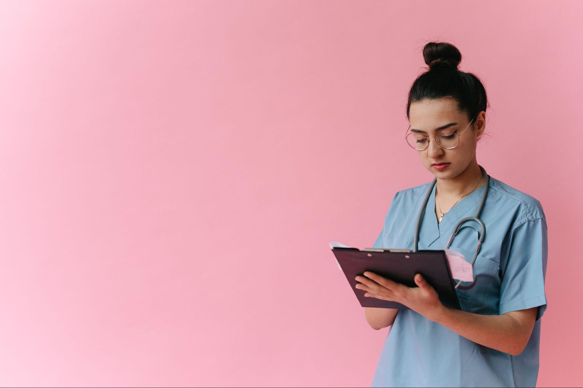Nurse writing on clipboard against a pink background