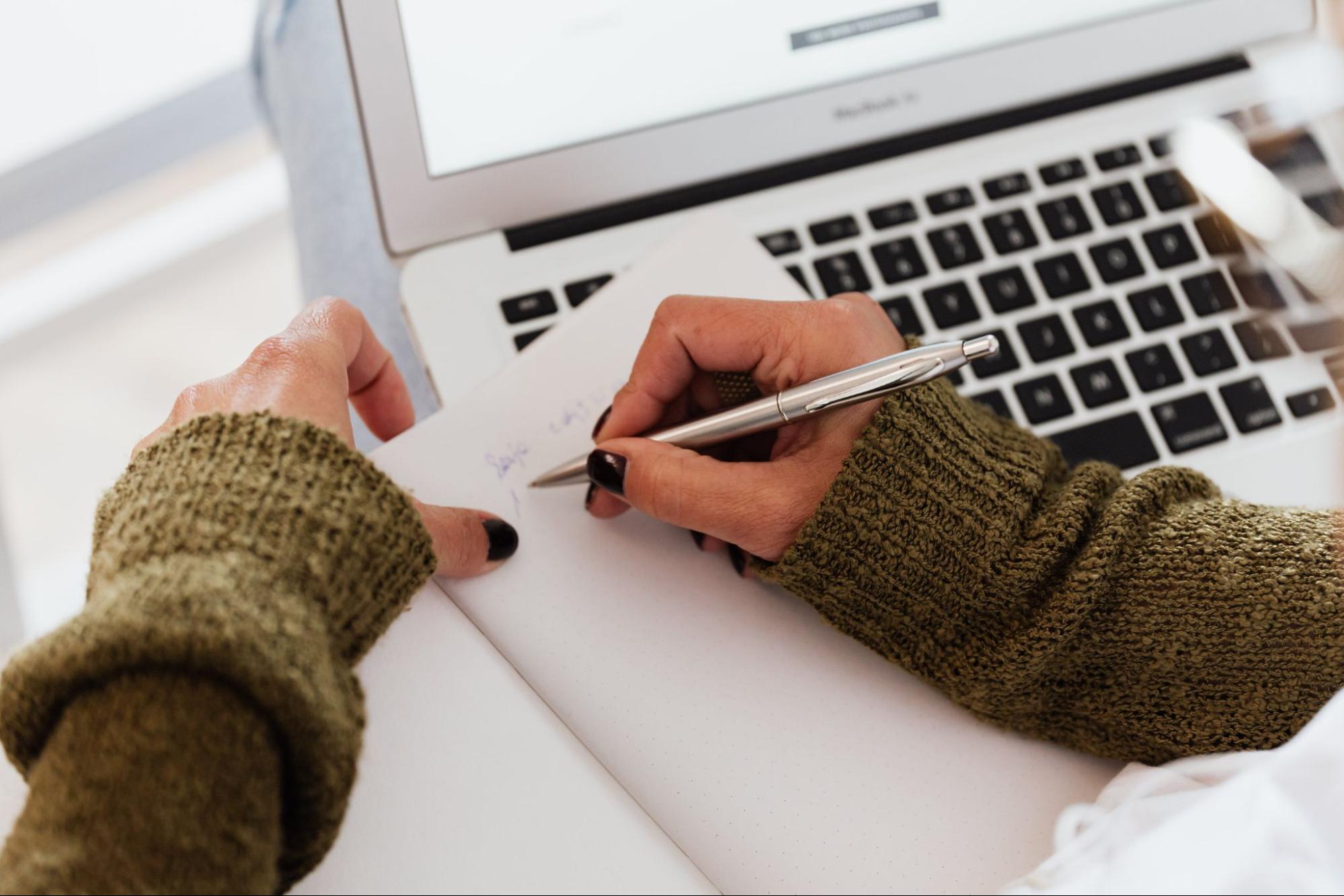 Person writing on paper in front of computer