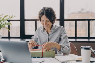 Woman unwrapping employee appreciation gift at desk in front of laptop