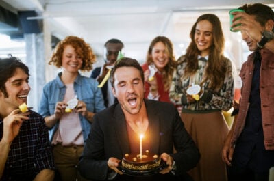 Person blowing out candle on work anniversary cake in office
