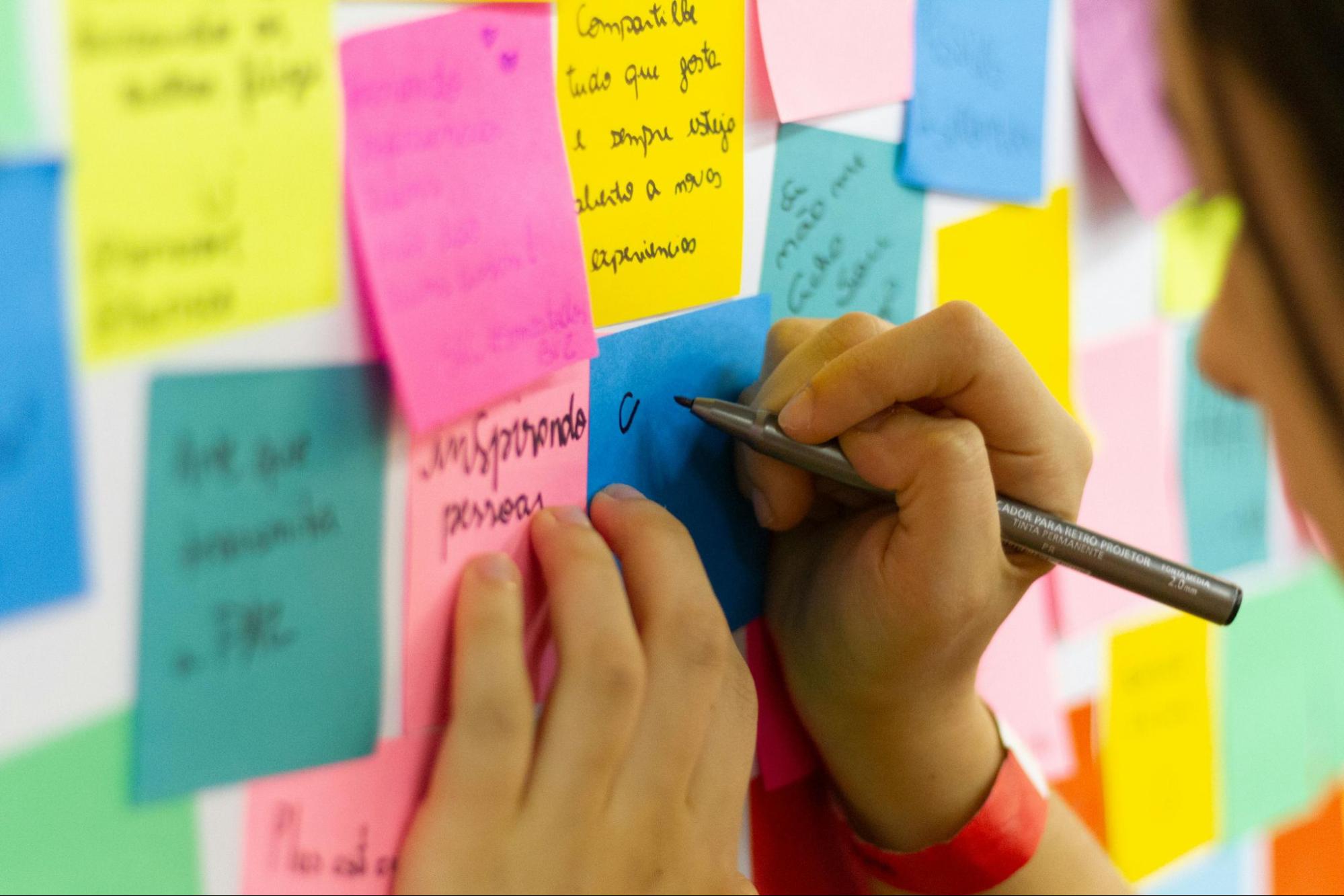 Person writing on post it note on an employee recognition board