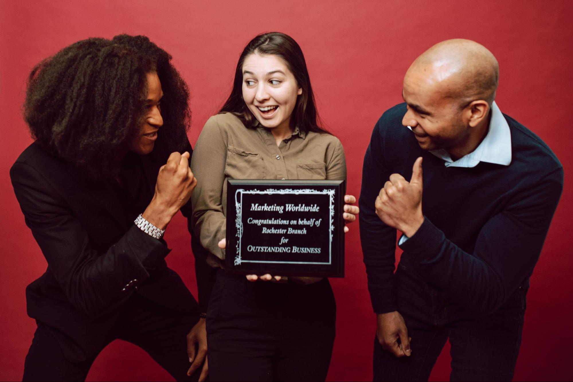 Woman holding employee award with coworkers giving her thumbs up