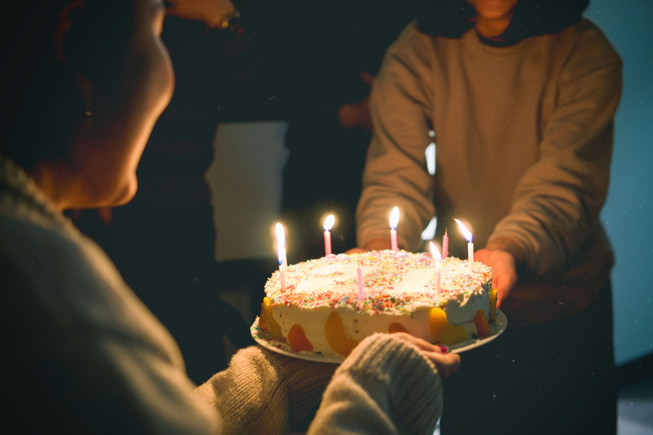 Person giving birthday cake lit with candles