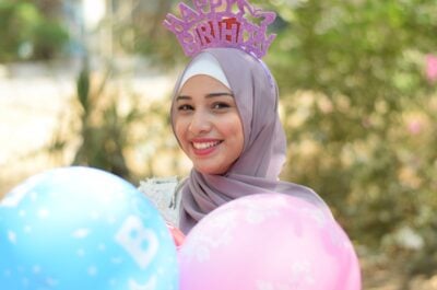 Woman wearing headscarf holding balloons and wearing birthday crown
