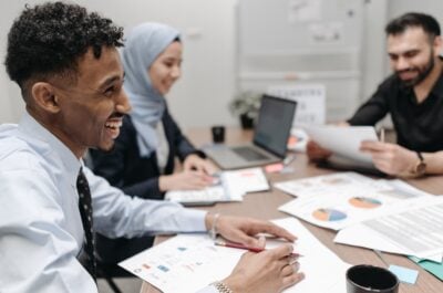 Close up of employee smiling and talking with others around desk