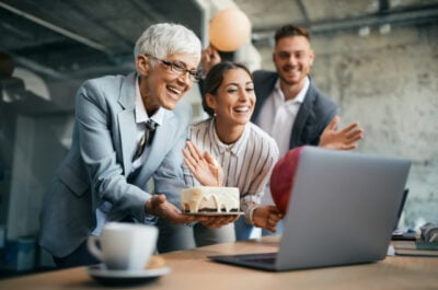 CEO with birthday cake celebrating with virtual and in-person employees