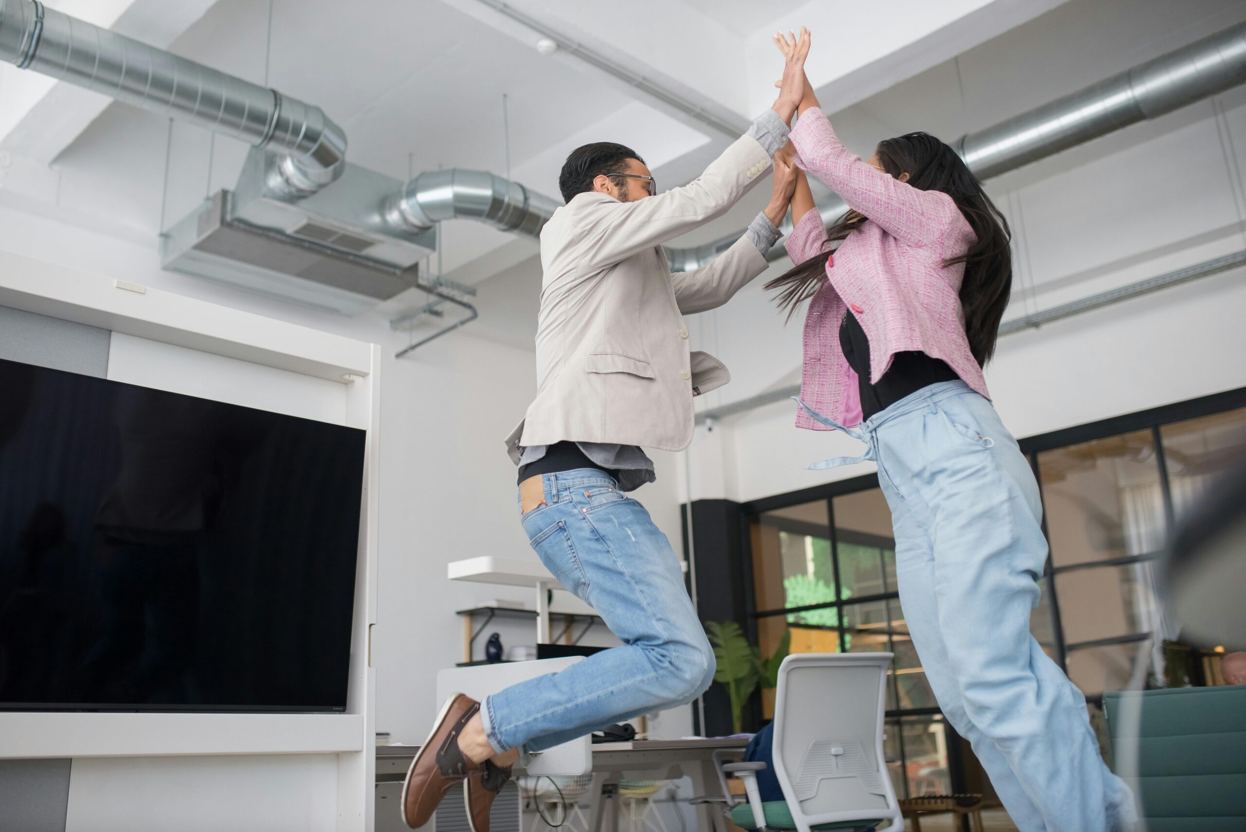 Two people wearing blue jeans high fiving thanks to employee recognition