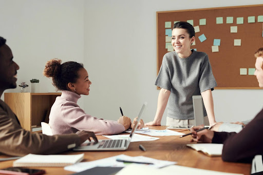 Measuring employee engagement is easy in workplaces like this one featuring a woman at the head of a board table smiling looking at other smiling, engaged employees.