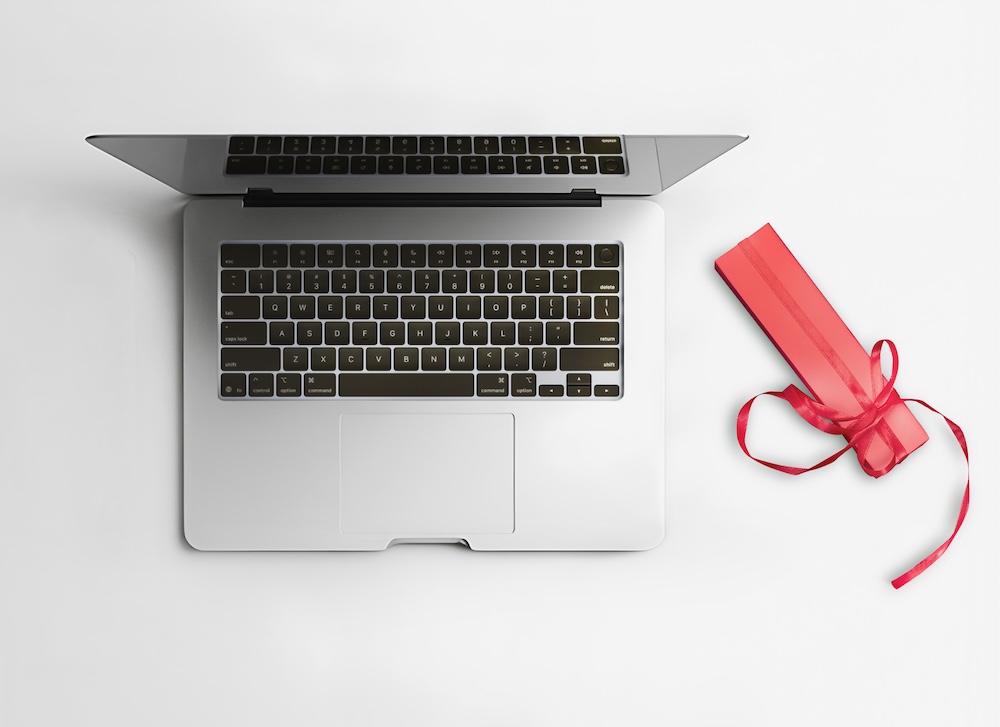 Overhead of a laptop with a group gift wrapped in red paper next to it.