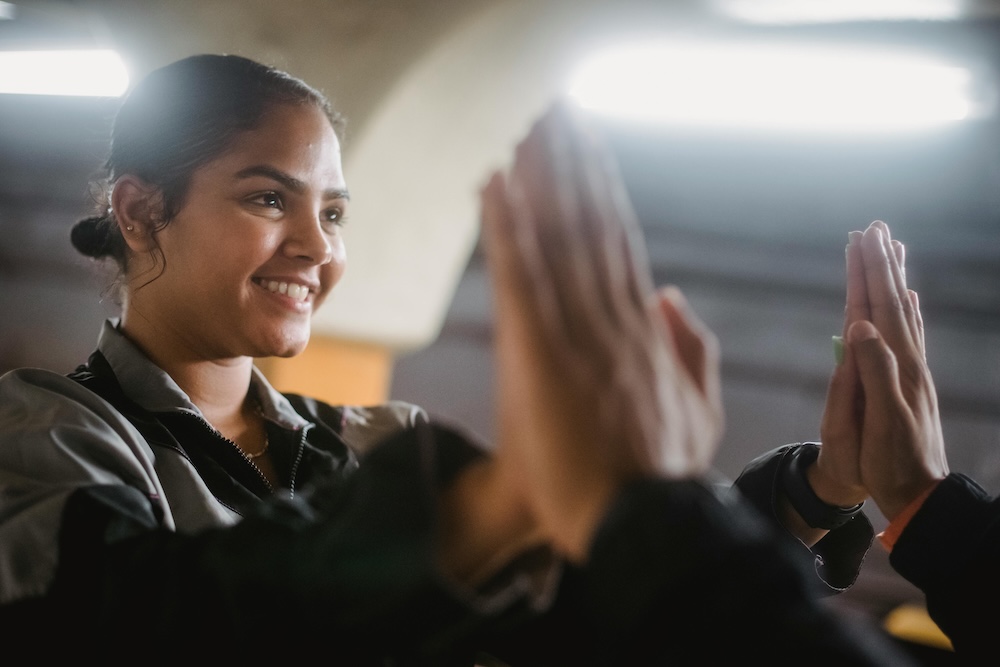 A smiling woman high fiving another person offscreen as part of employee recognition