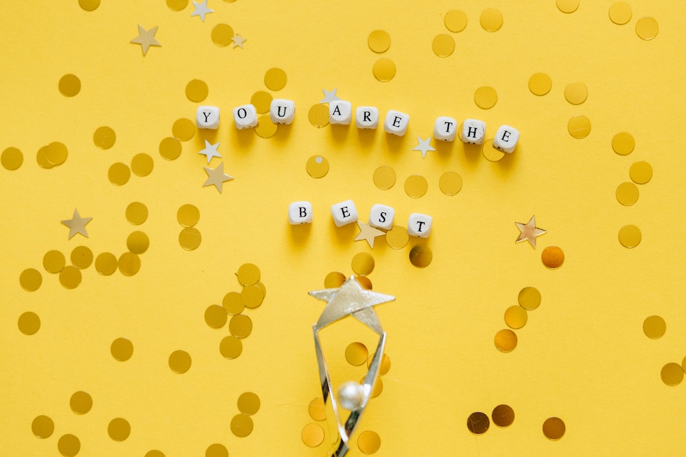 A yellow background with gold confetti, the top of a trophy, and