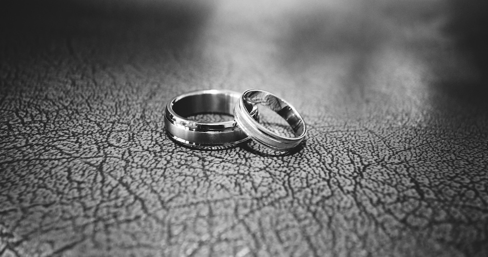 In black and white, two engagement rings are shown on a mottled/speckled foreground.