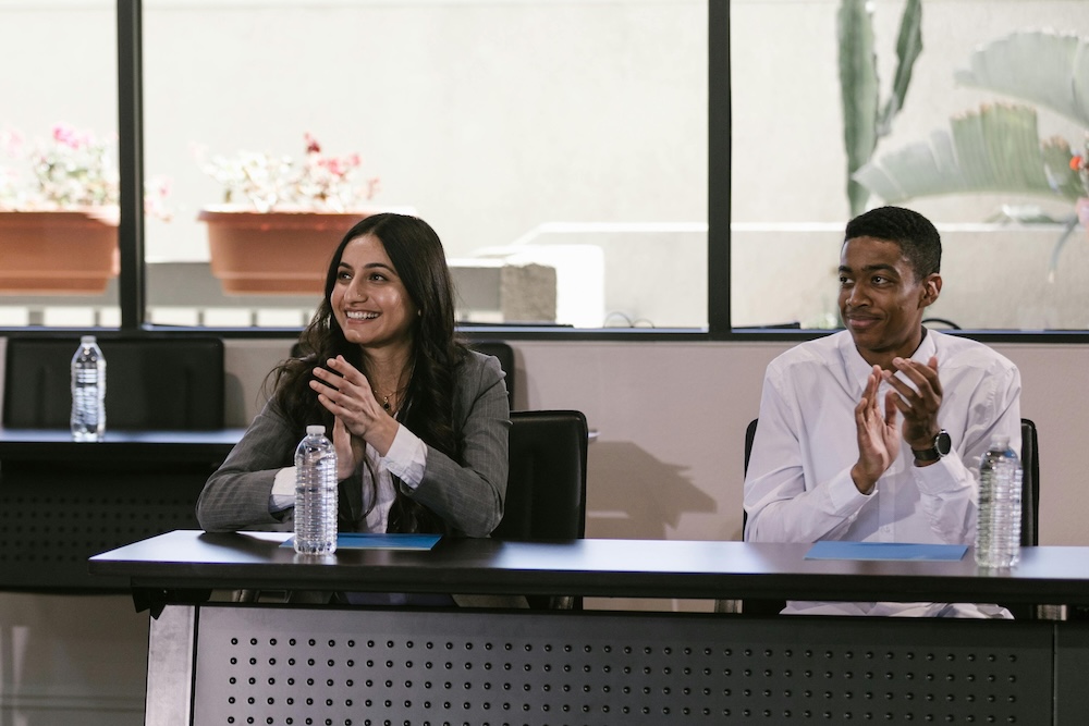 Employee recognition in the form of two smiling employees clapping at a desk