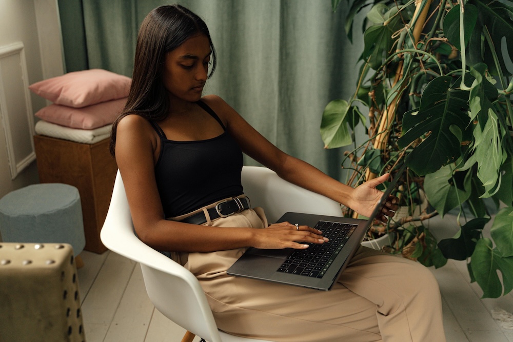 Gen Z woman sitting in a chair alone working on a laptop on employee recognition