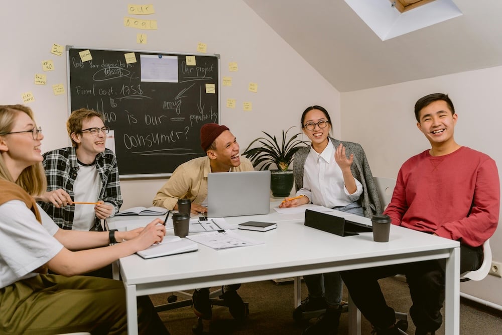 A group of young office workers around a meeting table, laughing at an ecard they received.