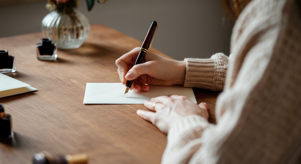 A hand writing maternity leave wishes on a desk
