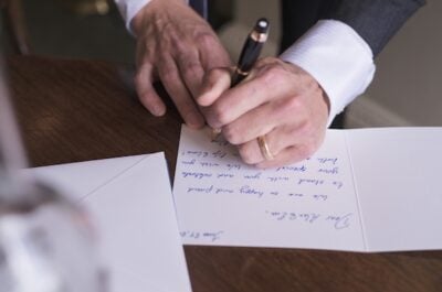 Left handed man wearing tuxedo and ring is writing a group greeting card.