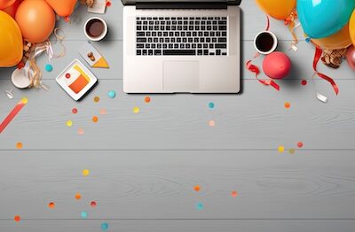 Overhead shot of a laptop with balloons and confetti with a happy work anniversary card