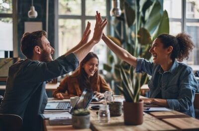 Peer to peer benefits like high fives from two employees while a third smiles in between in the background