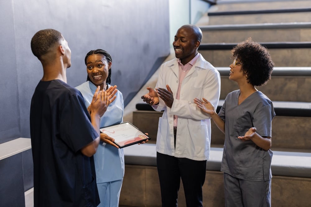 Four smiling medical professionals standing around laughing with clipboards celebrating eCards and employee recognition
