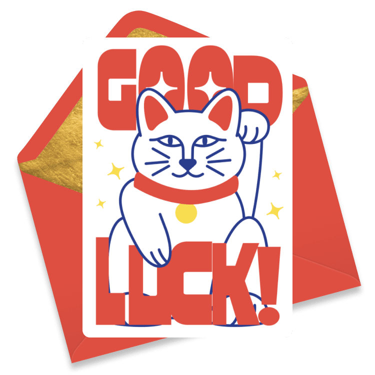 Cheerful farewell card with a lucky cat illustration and big red 'GOOD LUCK' lettering, set against a white background and resting on a red and yellow envelope.