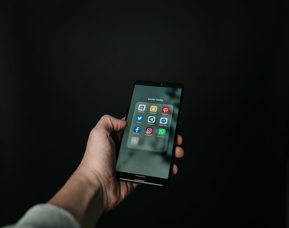 A hand holding out a phone with social media apps displayed on the screen