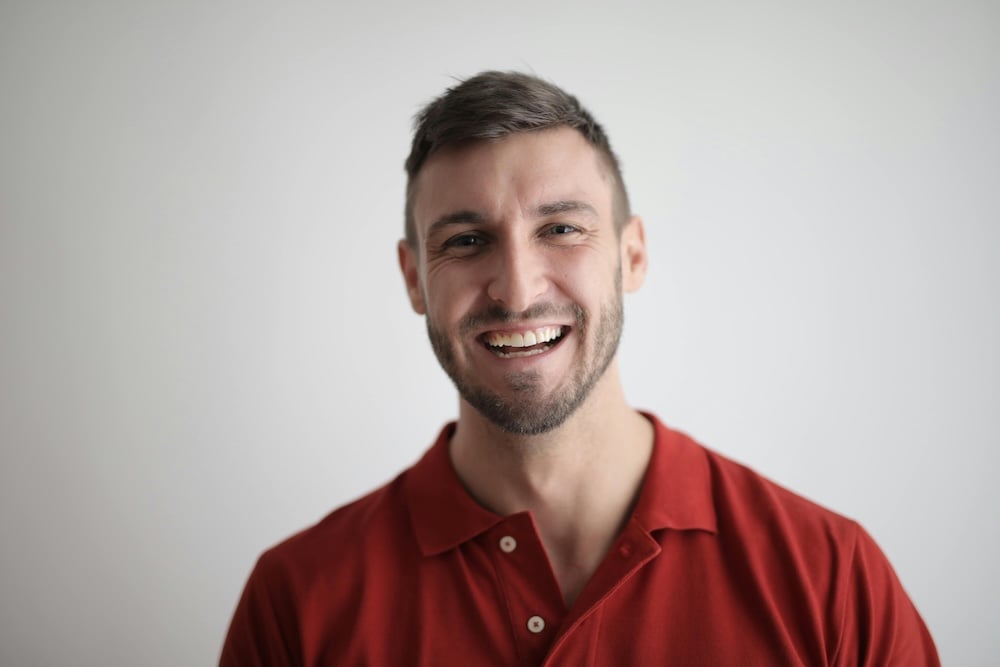 A man (perhaps someone's nephew) in a red polo shirt, smiling joyfully at the camera, on a plain white background