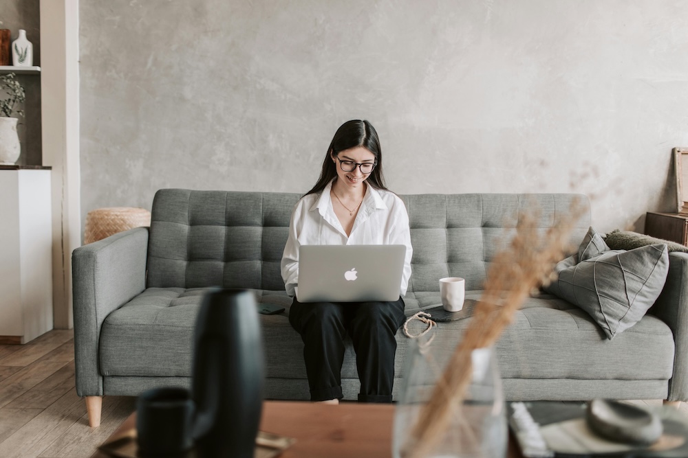 Smiling woman sitting on her laptop on a couch looking at ecards for employee recognition