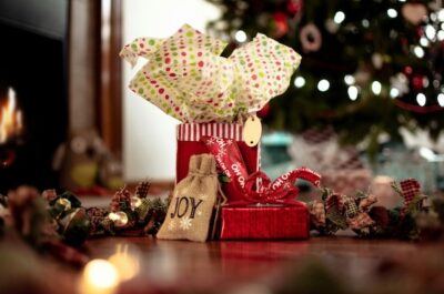 A festive holiday gift tableau, showing a cloth garland, wrapped gifts. A Christmas tree is shown twinkling faintly in the background.