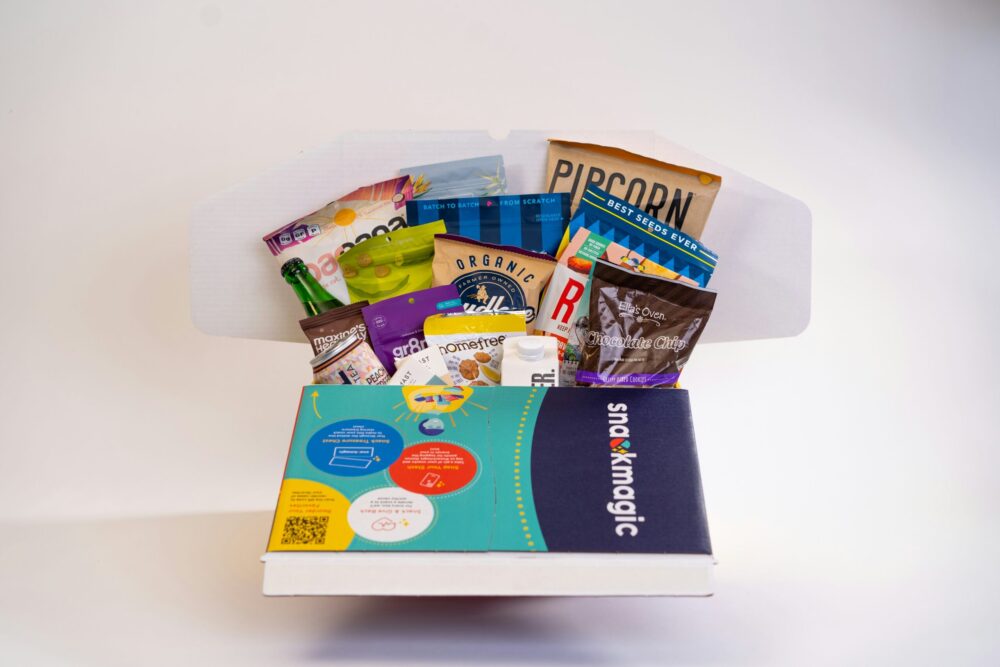 A delightful snack box holiday gift by Snackmagic, with packages of various snacks displayed emerging from the box.
