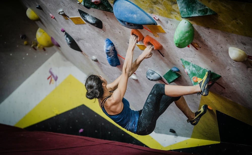Experiencing a unique Christmas gift, a woman hangs from a colorful rock-climbing wall.