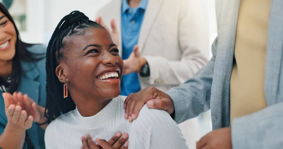 Businesswoman smiling as coworkers clap and support her, showing recognition that helps reduce anxiety at work and build belonging.