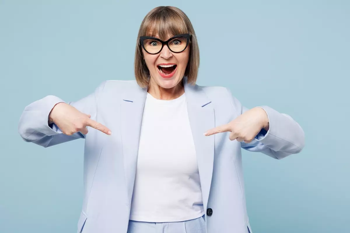 Confident employee spotlight image of a woman in a light blue suit, proudly pointing at herself against a simple studio background