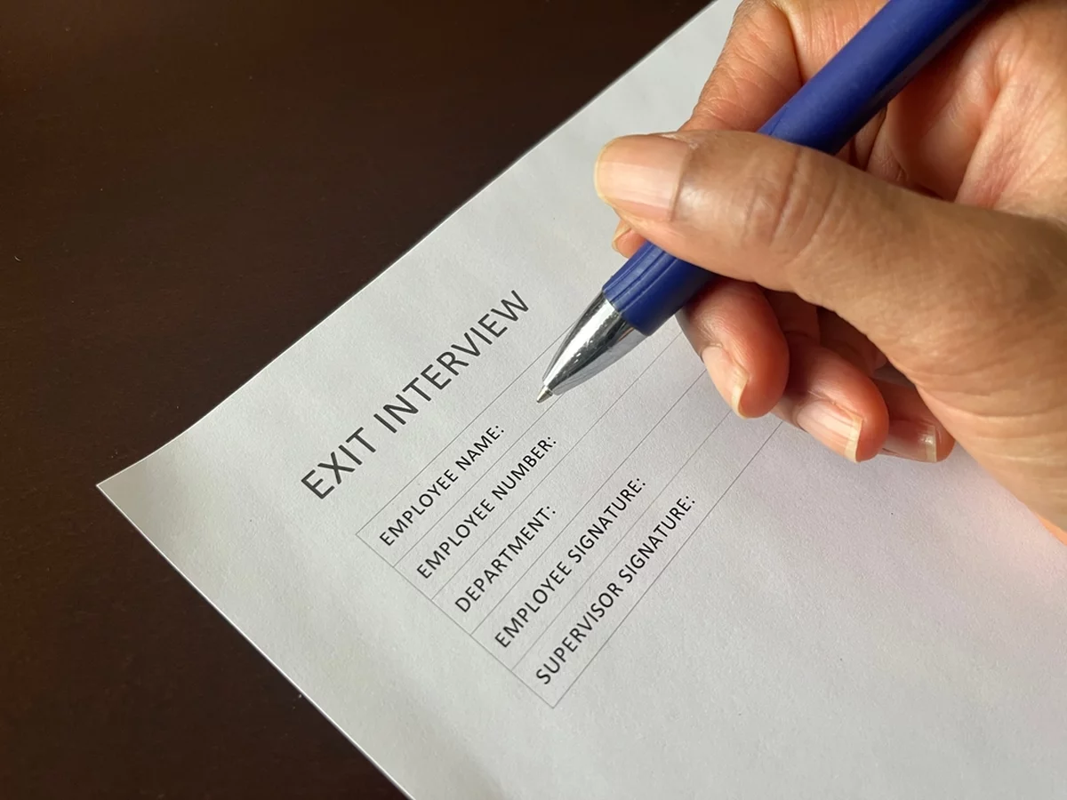 A resigning employee fills out a form, wondering if better exit interview questions could have helped this process.