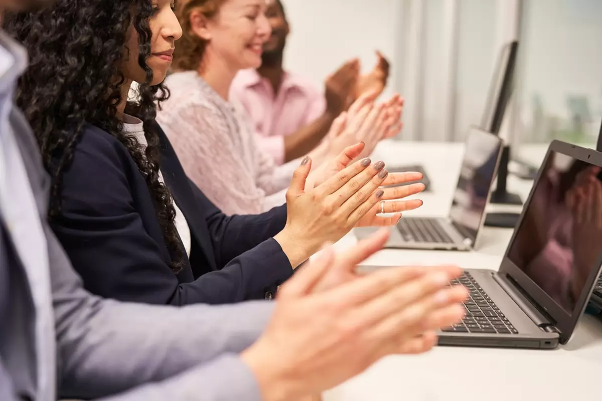 Office employees clapping in recognition with Kudo board; one of many valuable internal communication tools.
